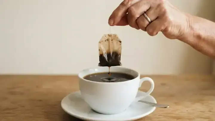A tea bag lifted from a porcelain cup of dark roasted tea, slow zoom